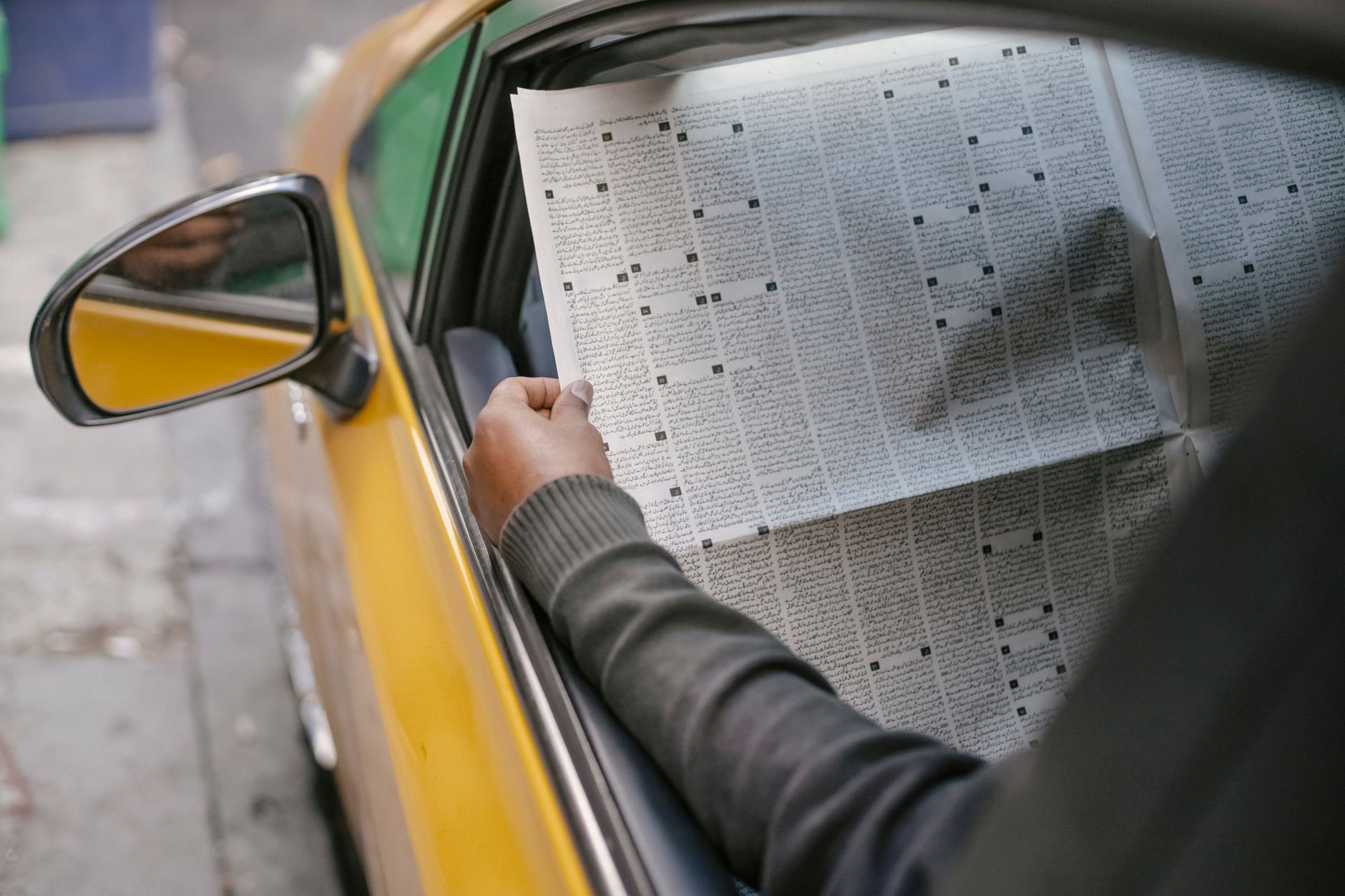 Crop unrecognizable person reading daily newspaper while sitting in car with opened window — Die besten Angebote: Boni und Ak