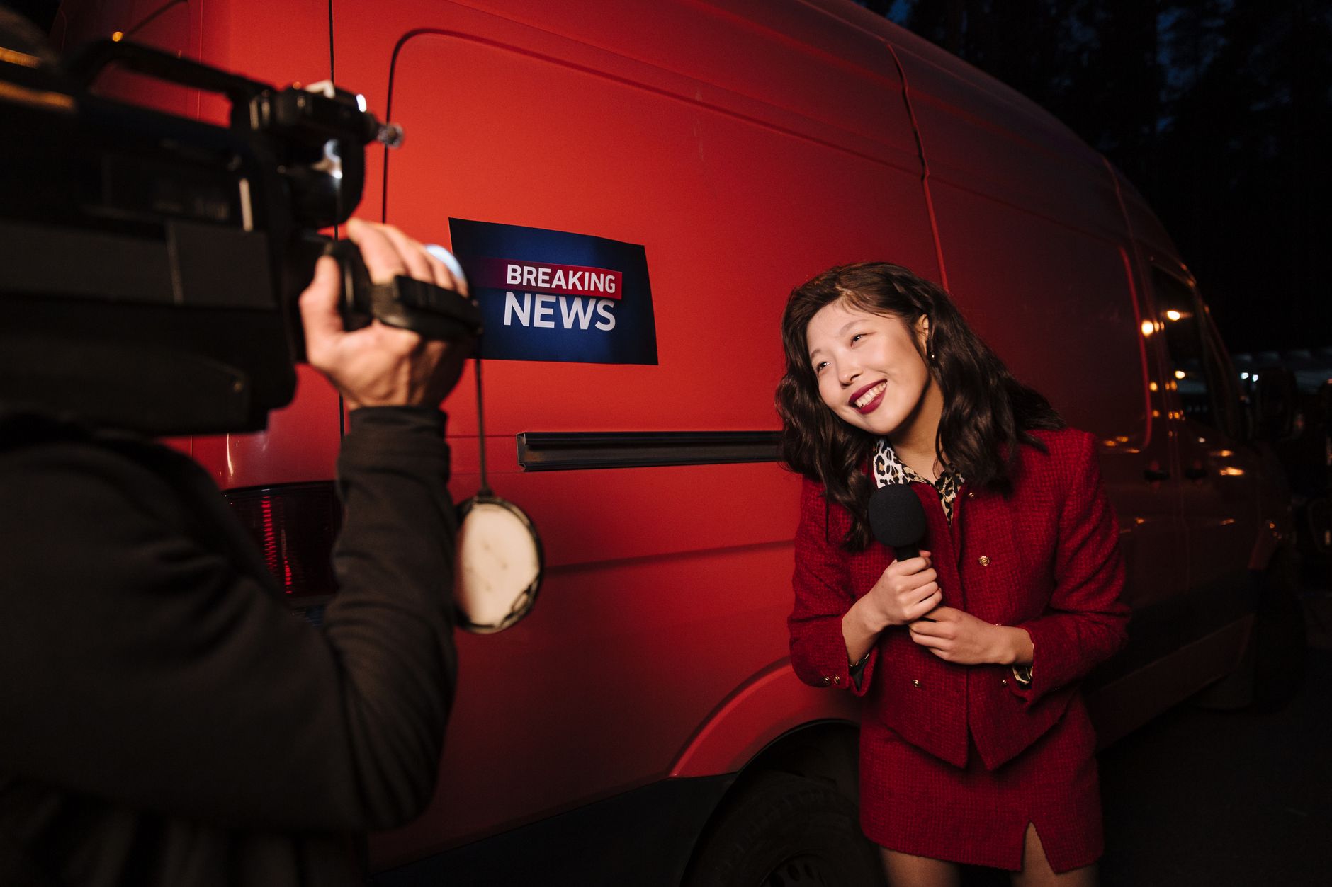 Asian female reporter in a red blazer reporting live on the news outdoors in the evening. — Die Einzigartigkeit von Spinight