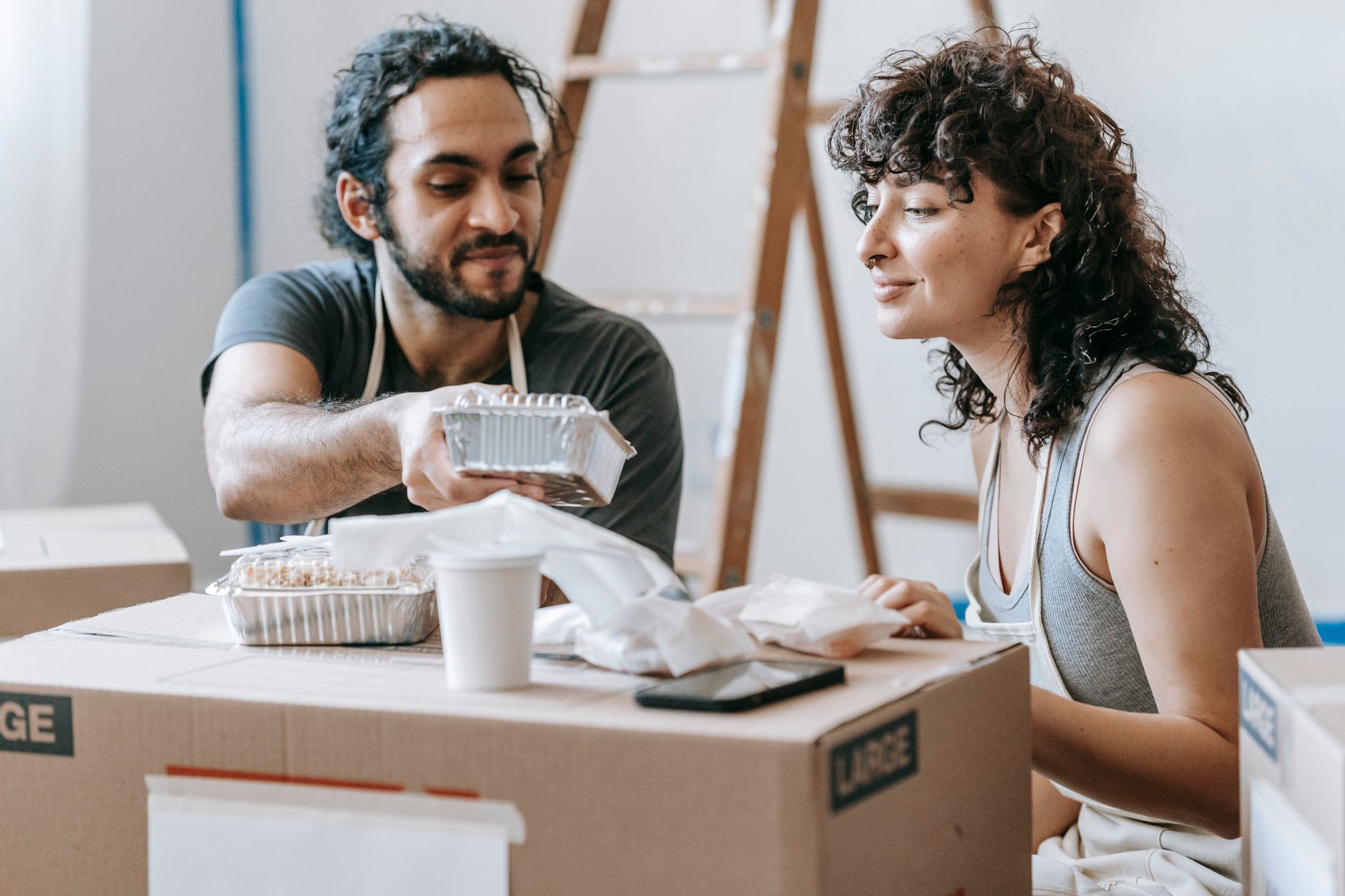 A couple relaxes with takeout food amidst moving boxes in their new home. — Erfahrungen mit dem mobilen Casino von Froggybet