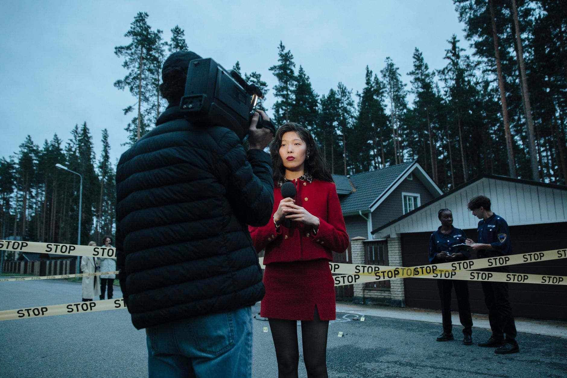 A female journalist reports live from an outdoor crime scene, flanked by police officers and media personnel. — GDF Casino: T