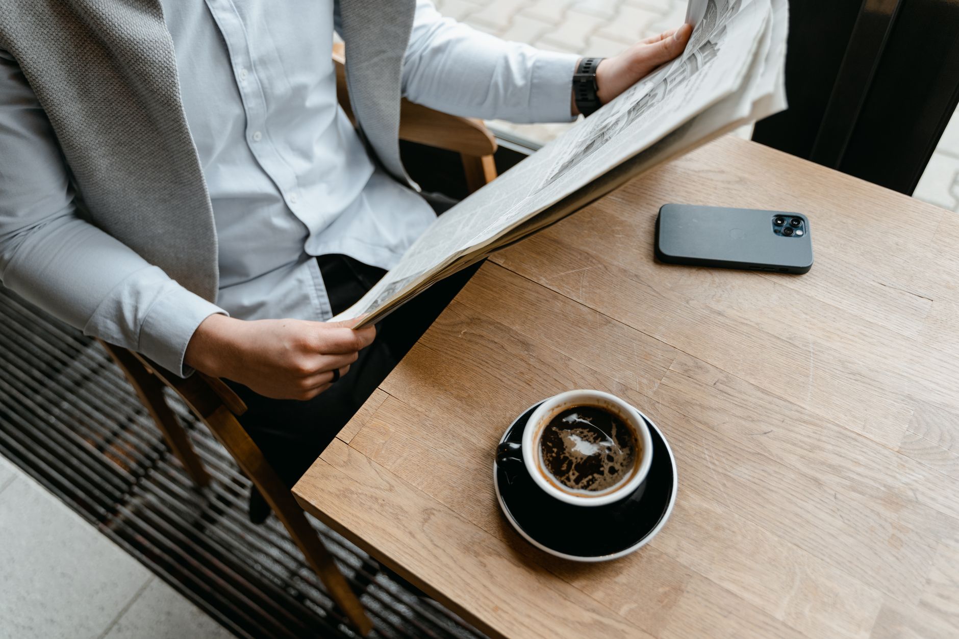 An adult male enjoying his coffee while reading a newspaper at a cafe with his smartphone nearby. — Instant Cash Out Casino: