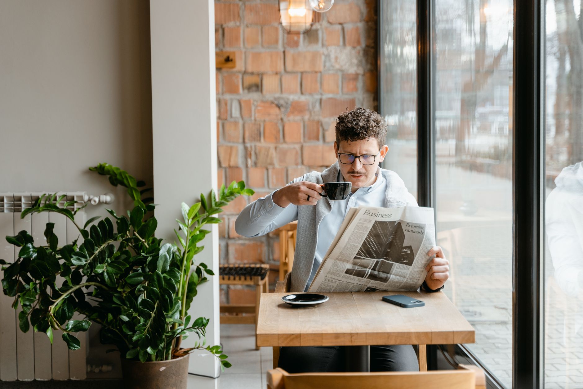 Man sitting indoors with coffee and newspaper, surrounded by plants by the window. — Warum ist die Registrierung im Rodeo Slo